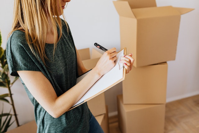 person writing an itemized list while packing things into boxes